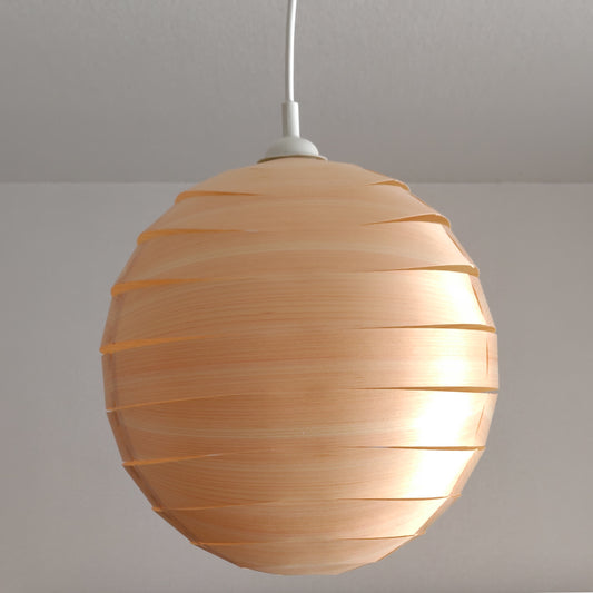 A brightly lit, spherical lampshade made of light brown wood veneer strips against a neutral wall. The overlapping curved pieces create a clean, modern, and geometric aesthetic.